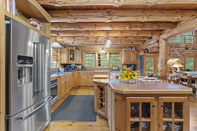 kitchen featuring light wood finished floors, light brown cabinets, a center island with sink, appliances with stainless steel finishes, and log walls