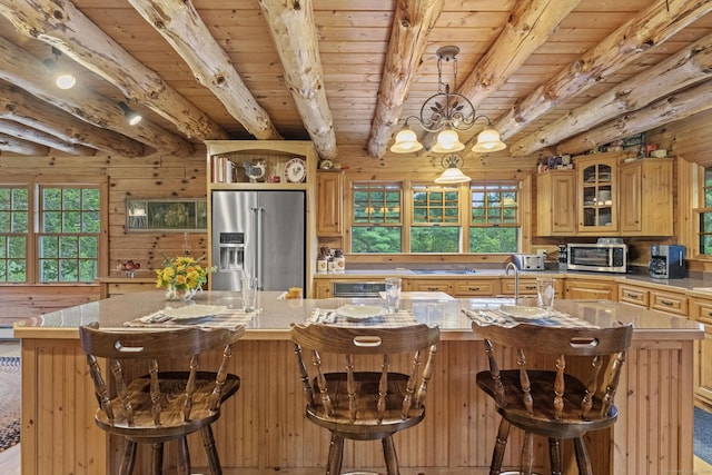 kitchen featuring beam ceiling, a center island with sink, white electric cooktop, stainless steel refrigerator with ice dispenser, and wooden walls