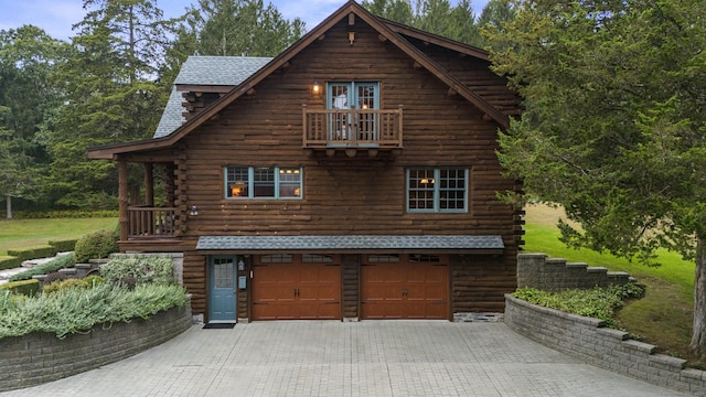 view of front of home featuring an attached garage, a balcony, log exterior, and decorative driveway
