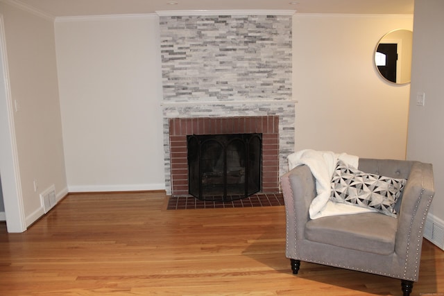 interior space with wood finished floors, a fireplace, visible vents, baseboards, and ornamental molding