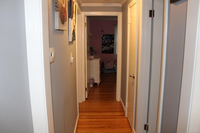 hall featuring light wood finished floors, ornamental molding, and baseboards