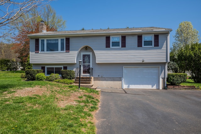 bi-level home featuring an attached garage, a front yard, driveway, and a chimney