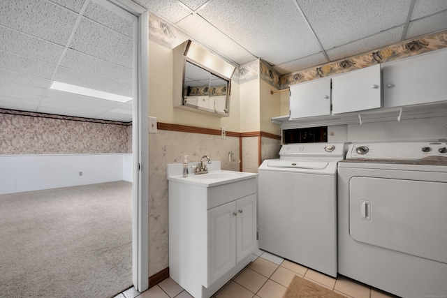 washroom featuring wallpapered walls, washer and clothes dryer, a wainscoted wall, a sink, and cabinet space