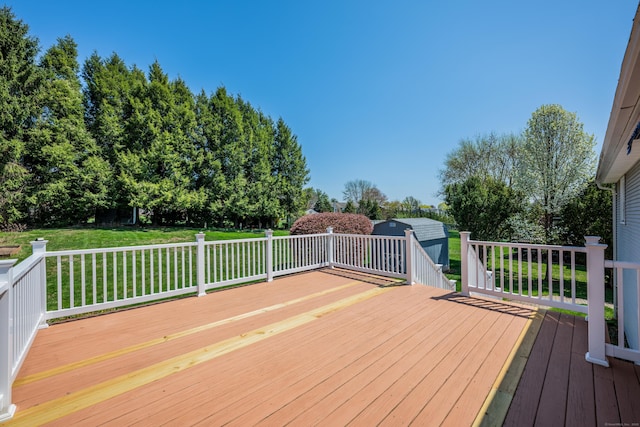 wooden terrace featuring a lawn, a shed, and an outbuilding