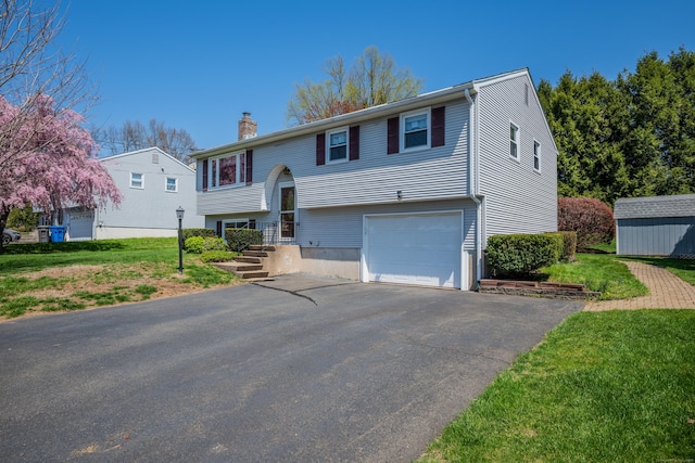 split foyer home featuring an outdoor structure, a front lawn, a chimney, an attached garage, and driveway
