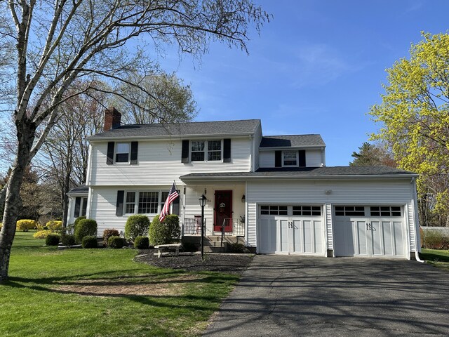 view of front facade featuring a front lawn, a chimney, aphalt driveway, and a garage