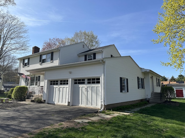 exterior space with a front lawn, a chimney, a garage, and aphalt driveway