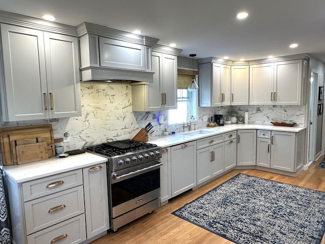 kitchen featuring stainless steel stove, gray cabinets, backsplash, and a sink