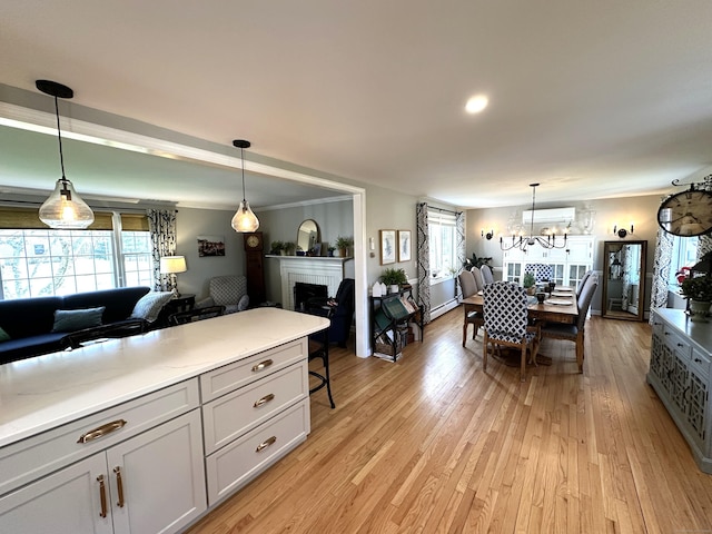 dining area with a wall mounted AC, a fireplace, an inviting chandelier, and light wood-style flooring