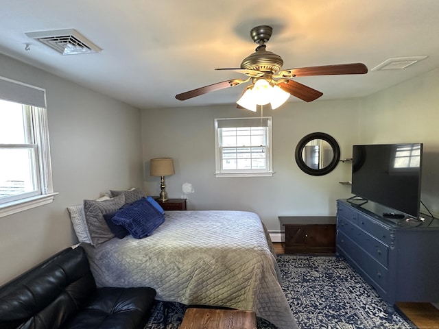 bedroom featuring visible vents, ceiling fan, a baseboard heating unit, baseboards, and wood finished floors