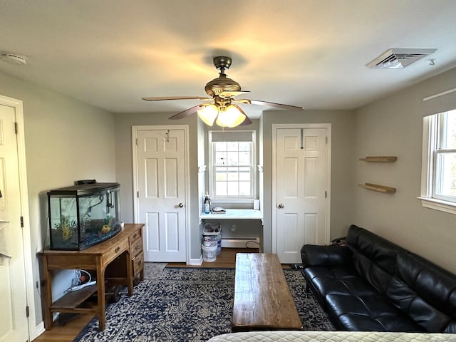 living area with baseboard heating, ceiling fan, dark wood-style flooring, and visible vents