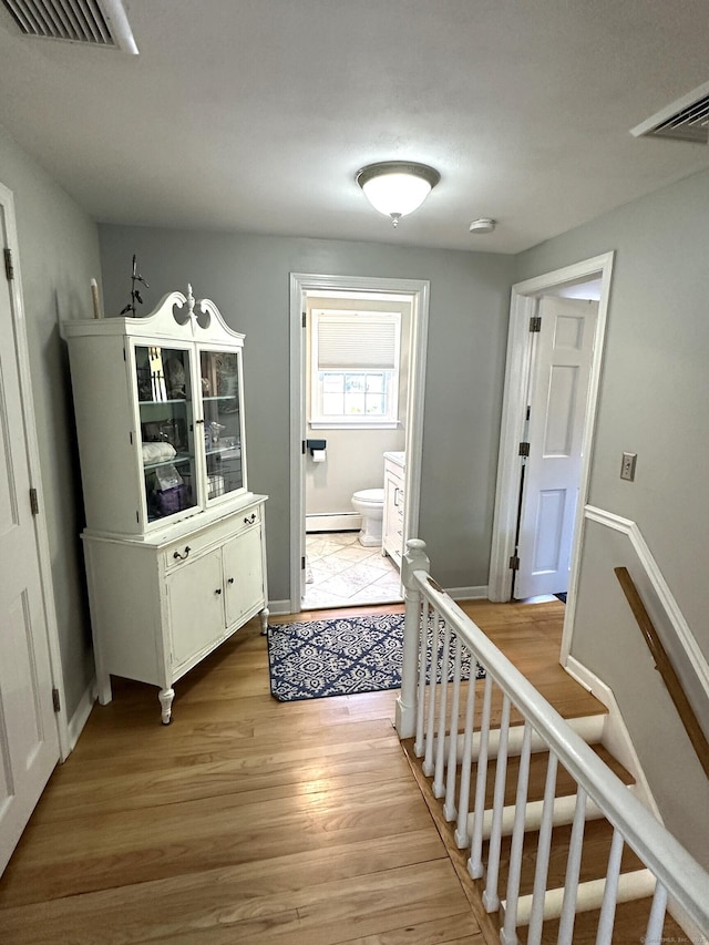 hallway with light wood finished floors, baseboards, baseboard heating, and visible vents