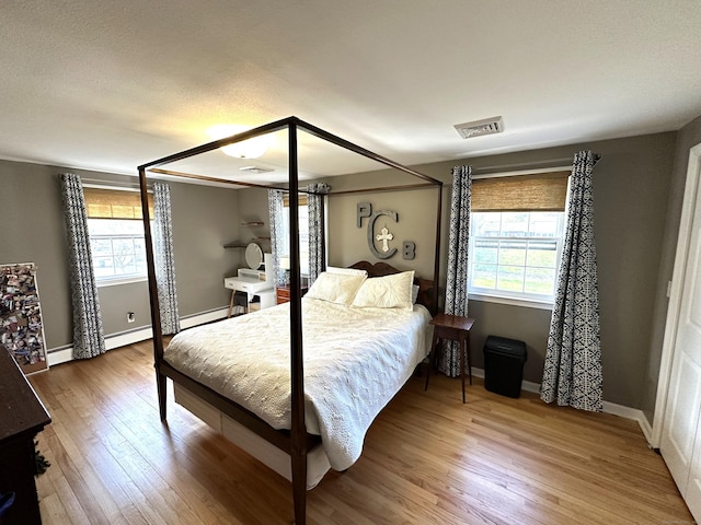 bedroom with visible vents, baseboards, wood finished floors, and a baseboard radiator