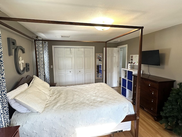 bedroom with wood finished floors, visible vents, and a closet