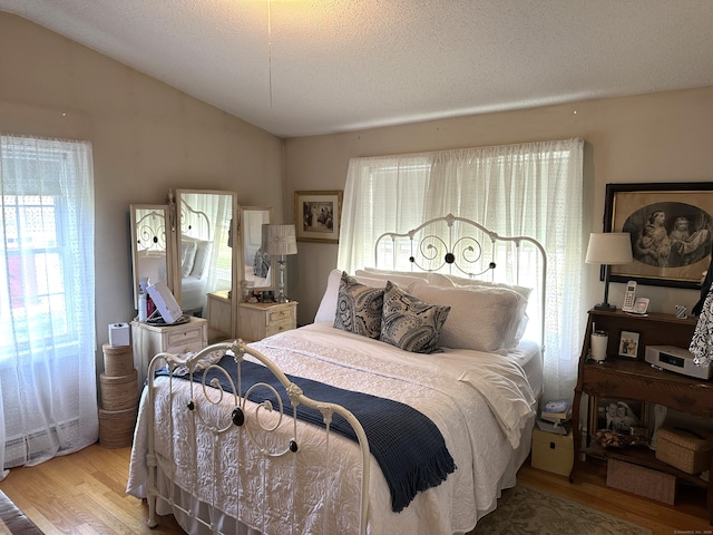 bedroom featuring vaulted ceiling, wood finished floors, and a textured ceiling