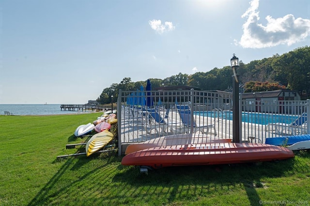 community pool with a water view, fence, and a yard