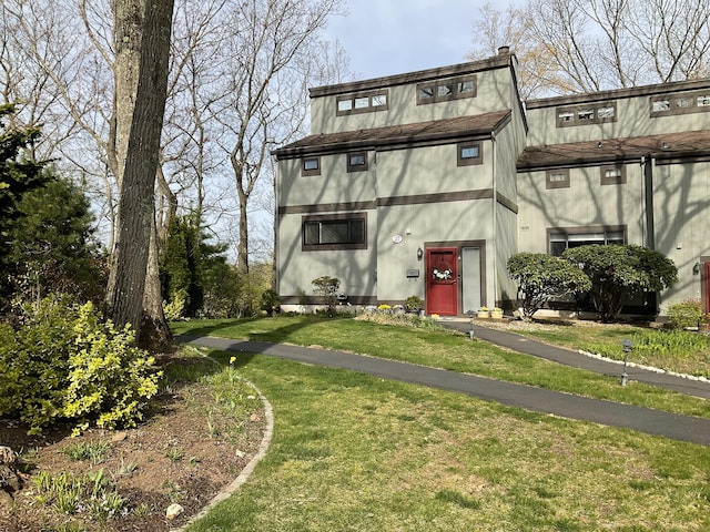 view of front of home featuring a chimney, roof with shingles, and a front yard