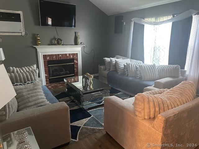 living area featuring vaulted ceiling, wood finished floors, a brick fireplace, and a wall mounted air conditioner
