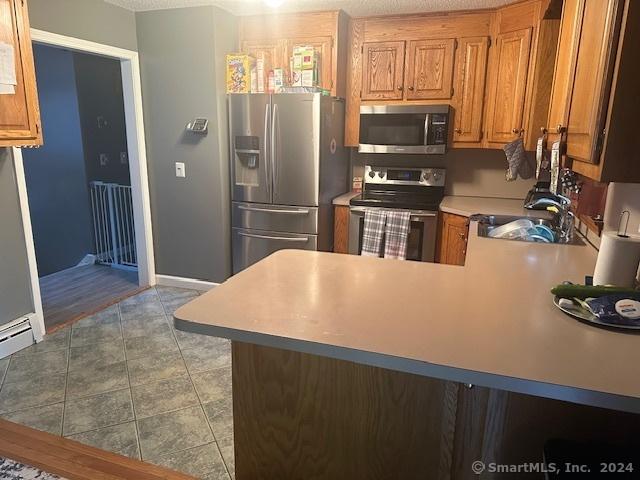 kitchen with a sink, brown cabinets, stainless steel appliances, light countertops, and a peninsula