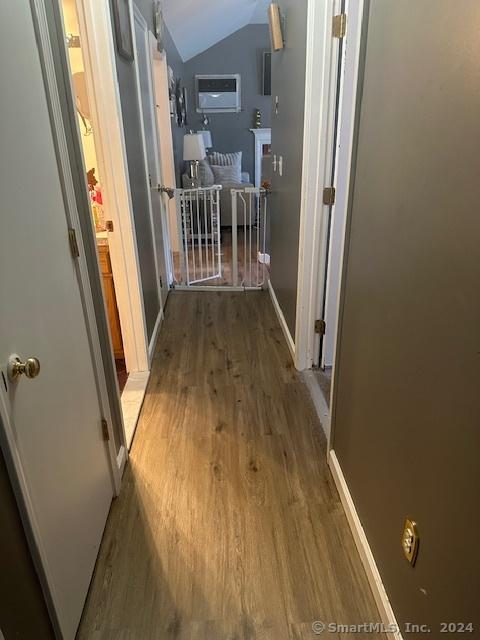 corridor featuring vaulted ceiling, wood finished floors, and baseboards