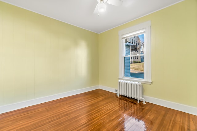 spare room featuring a ceiling fan, radiator heating unit, hardwood / wood-style floors, baseboards, and ornamental molding