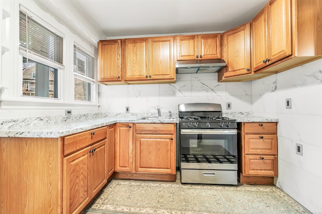 kitchen featuring light stone countertops, under cabinet range hood, a sink, and gas range