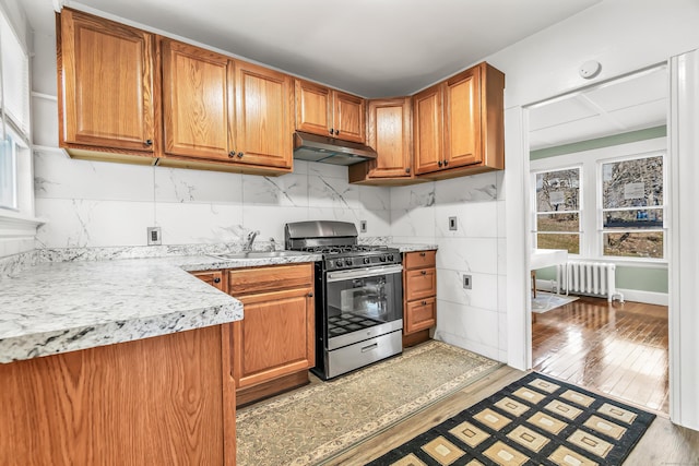 kitchen featuring stainless steel range with gas stovetop, radiator, light wood-style floors, light countertops, and under cabinet range hood