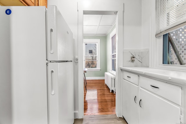 kitchen with radiator heating unit, light wood finished floors, light countertops, freestanding refrigerator, and baseboards