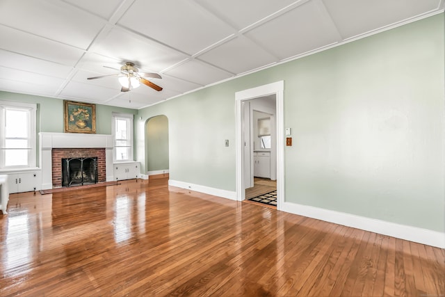 unfurnished living room featuring hardwood / wood-style floors, ceiling fan, arched walkways, a fireplace, and baseboards