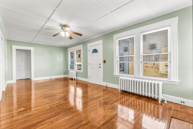 empty room featuring radiator heating unit, hardwood / wood-style floors, baseboards, and ceiling fan