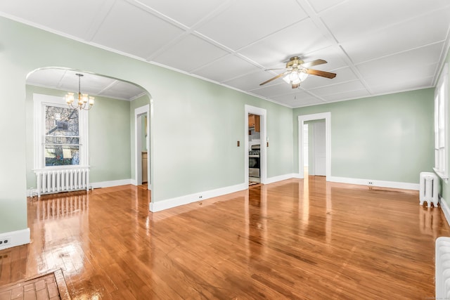 unfurnished living room with wood finished floors, ceiling fan with notable chandelier, arched walkways, radiator, and baseboards
