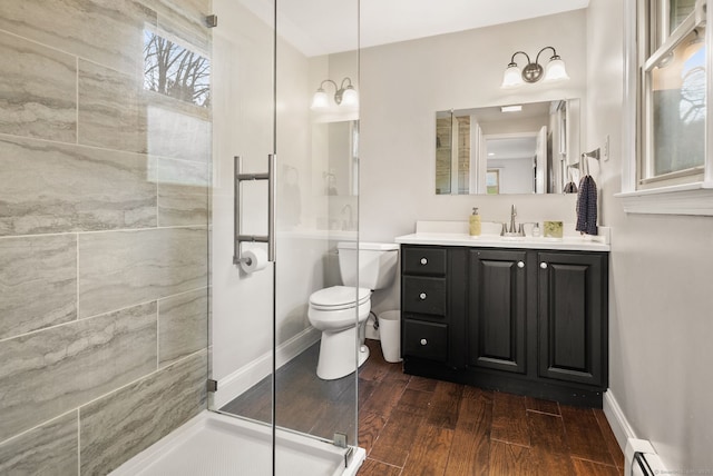 bathroom featuring vanity, wood finished floors, toilet, baseboard heating, and a walk in shower