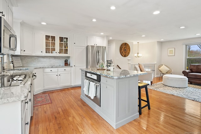 kitchen featuring decorative backsplash, a breakfast bar, white cabinets, light wood-style flooring, and appliances with stainless steel finishes