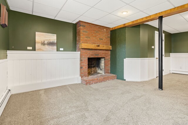 unfurnished living room with carpet, baseboard heating, wainscoting, and a drop ceiling