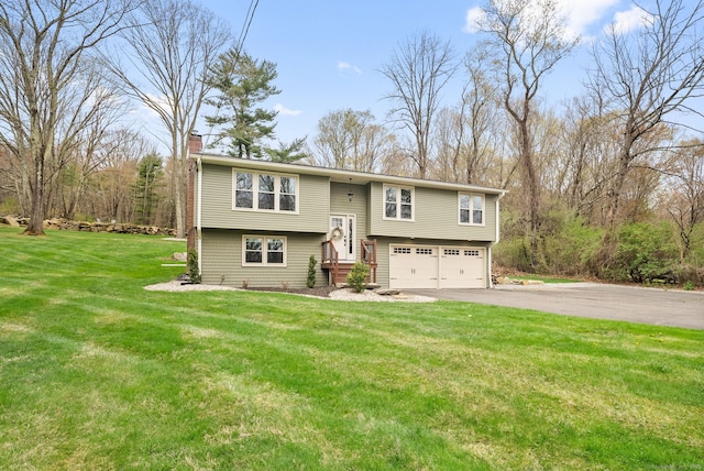 split foyer home with an attached garage, driveway, a chimney, and a front yard