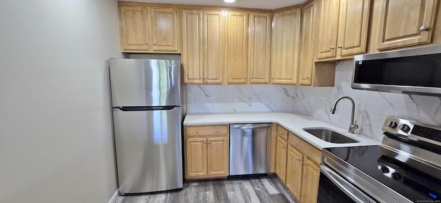 kitchen featuring appliances with stainless steel finishes, decorative backsplash, a sink, and light wood-type flooring