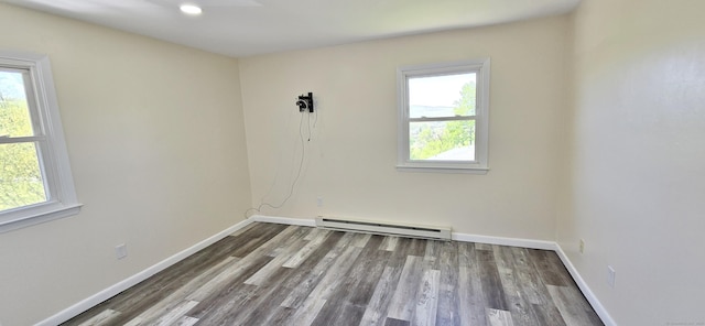 spare room with baseboards, a baseboard heating unit, a healthy amount of sunlight, and wood finished floors