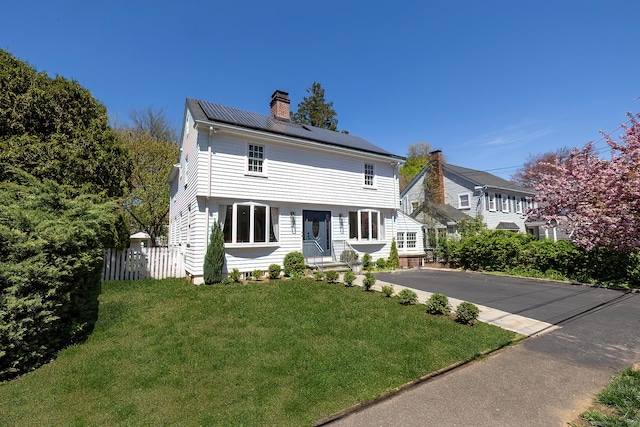 view of front of house with fence, solar panels, a front lawn, and a chimney