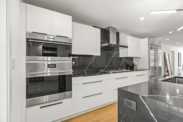 kitchen featuring wall chimney range hood, white cabinets, appliances with stainless steel finishes, tasteful backsplash, and modern cabinets