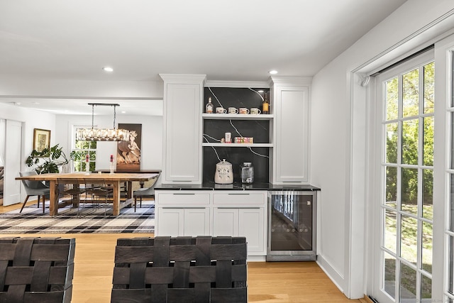 bar featuring light wood-style flooring, recessed lighting, decorative light fixtures, wine cooler, and a bar