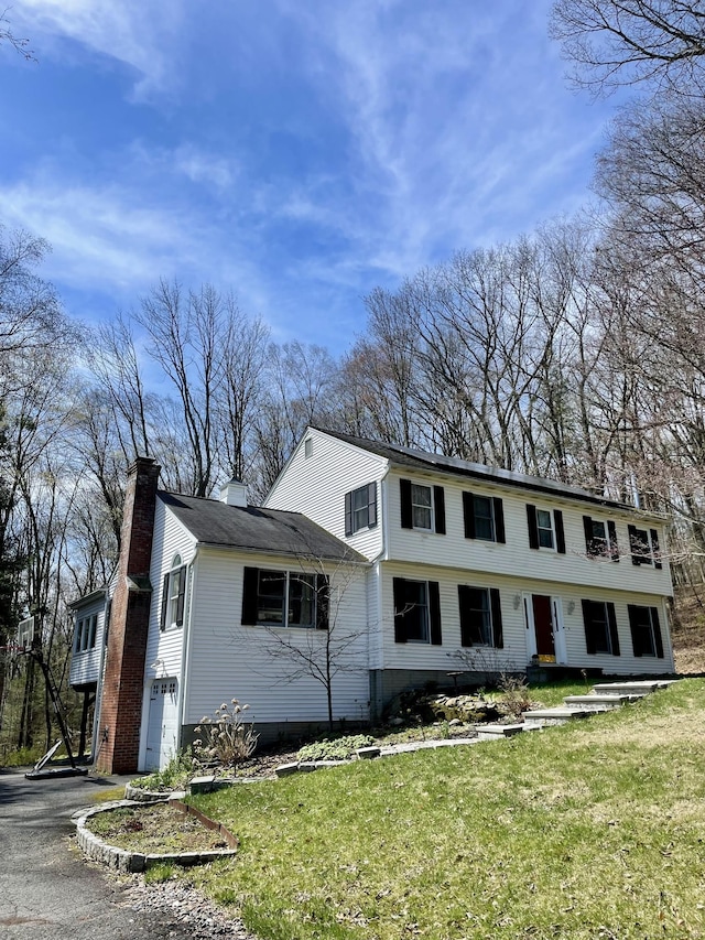 view of front facade with a chimney, aphalt driveway, a front yard, and an attached garage