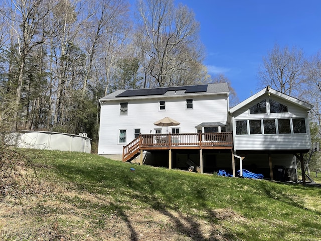 rear view of property with a yard, a deck, solar panels, and stairs