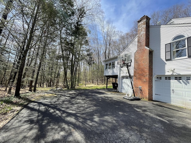 view of property exterior with a chimney, an attached garage, and driveway