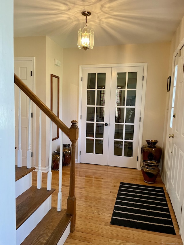 doorway to outside featuring french doors, light wood-style floors, a notable chandelier, and stairs