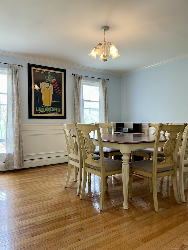 dining room featuring an inviting chandelier, light wood-style floors, crown molding, wainscoting, and baseboard heating