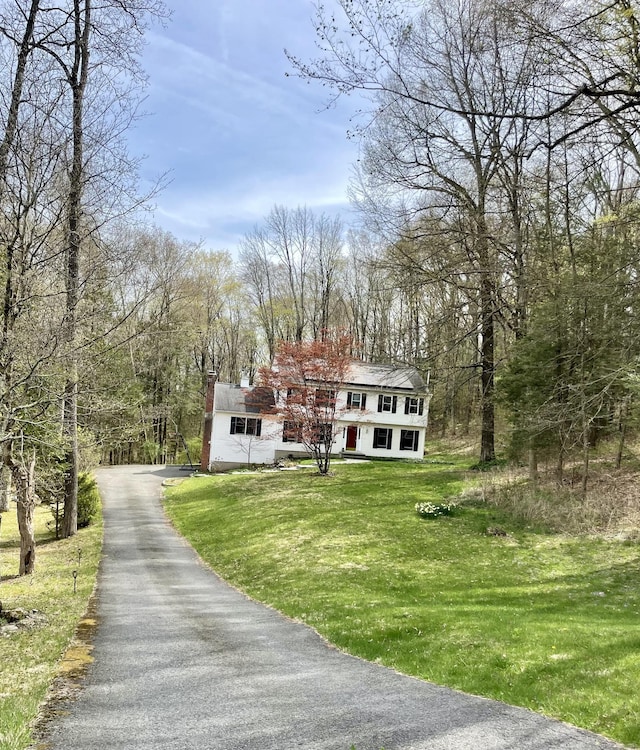 exterior space with a wooded view, aphalt driveway, and a front lawn