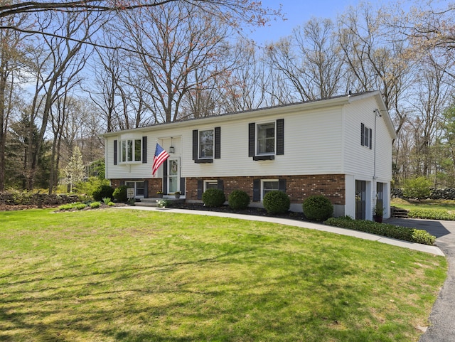 raised ranch featuring a front lawn, driveway, a garage, and brick siding
