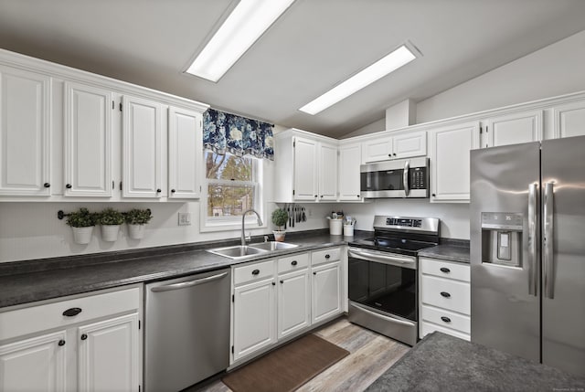 kitchen with appliances with stainless steel finishes, dark countertops, a sink, white cabinetry, and lofted ceiling