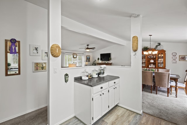 interior space featuring light wood-style floors, lofted ceiling with beams, baseboards, dark countertops, and white cabinets