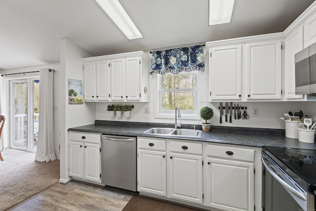 kitchen with white cabinetry, stainless steel appliances, dark countertops, and a sink